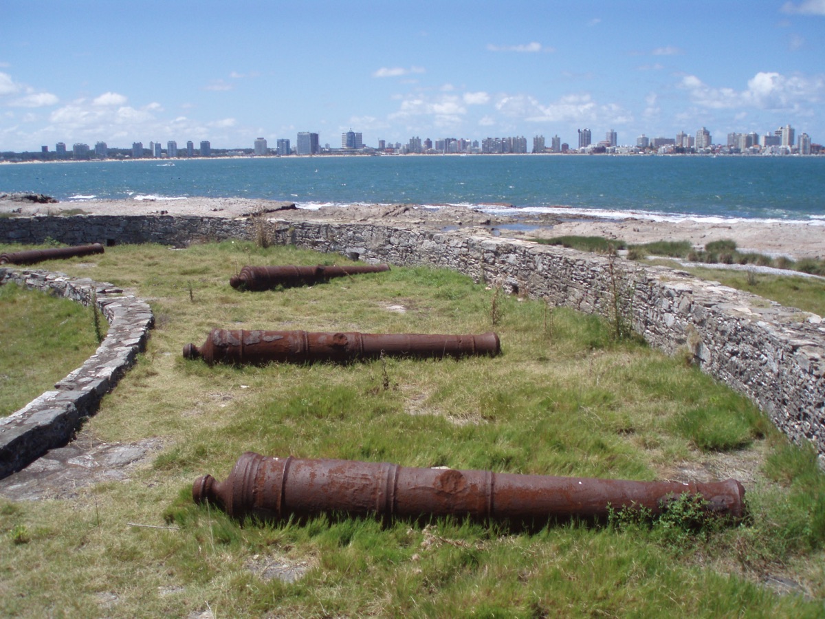 Cañones coloniales tumbados entre el pasto en la batería este de la Isla Gorriti, con las torres de Punta del Este al otro lado del agua