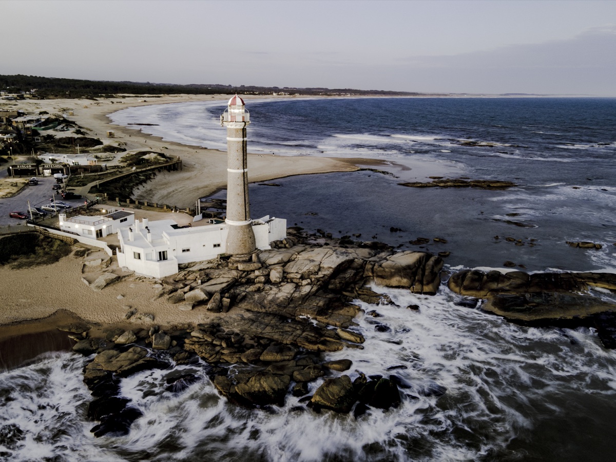 El faro de José Ignacio sobre la punta rocosa, con la arena curvándose a un lado y el oleaje rompiendo contra las piedras del otro