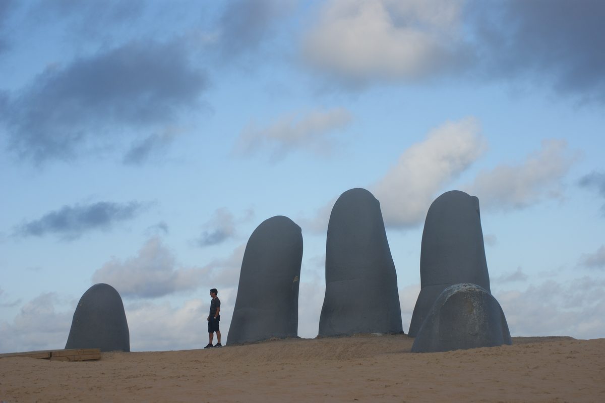 Los dedos de La Mano saliendo de la arena de la Playa Brava, con una persona caminando al lado que da la escala