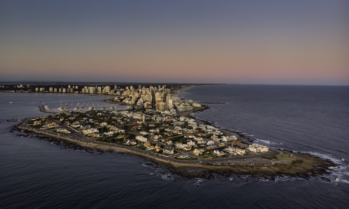 La península de Punta del Este desde el aire al atardecer: casas bajas y el faro en la punta, el puerto a la izquierda y las torres de la Playa Mansa detrás