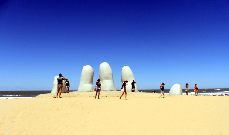 La arena de la Playa Brava llena de gente en un día de enero, alrededor de la escultura de La Mano