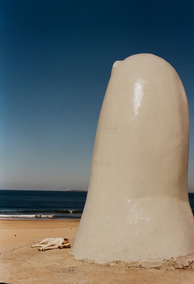 Uno de los dedos de La Mano de cerca en la Playa Brava, con un perro durmiendo a su sombra y el faro en el horizonte